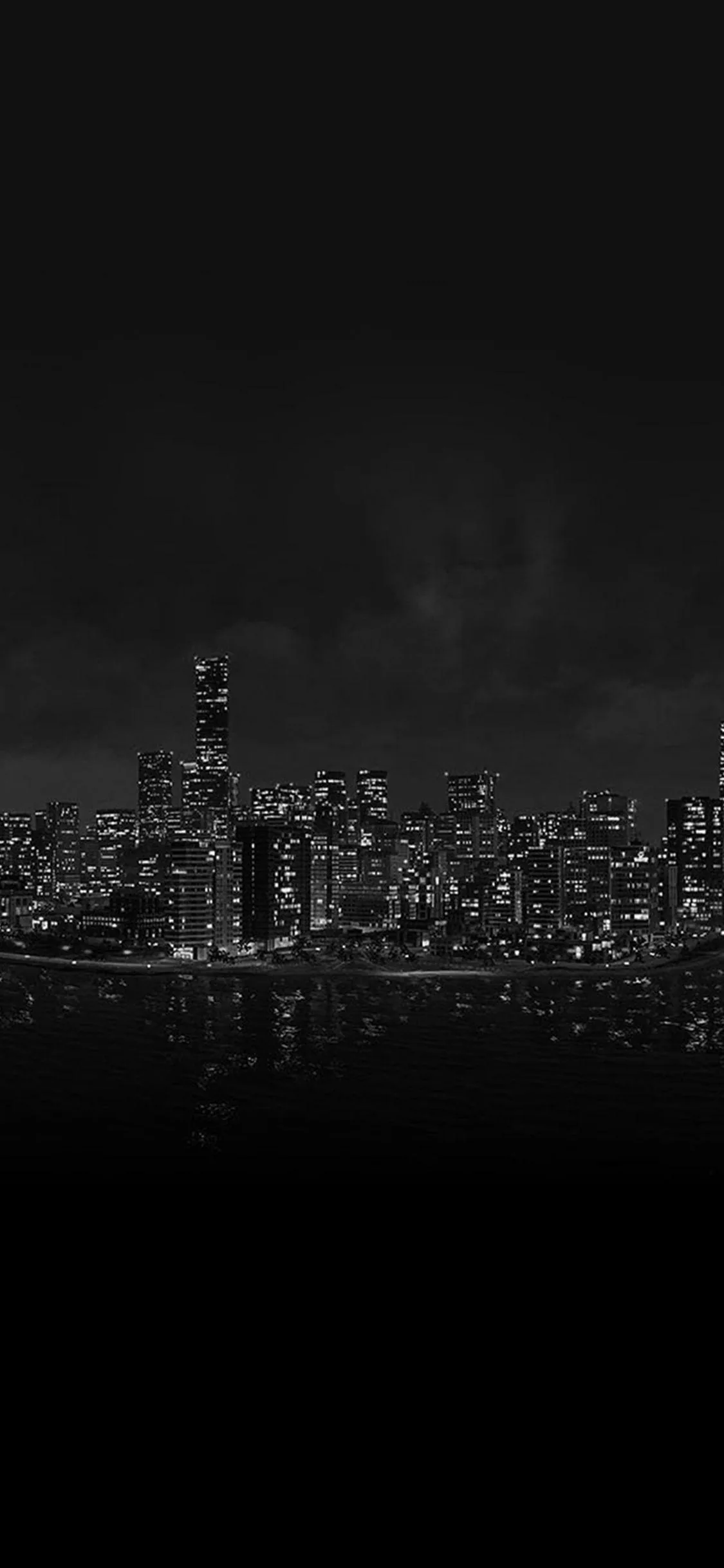 A row of lit towers sits low in the tall frame, its reflection breaking up in the water while the sky above stays near black.