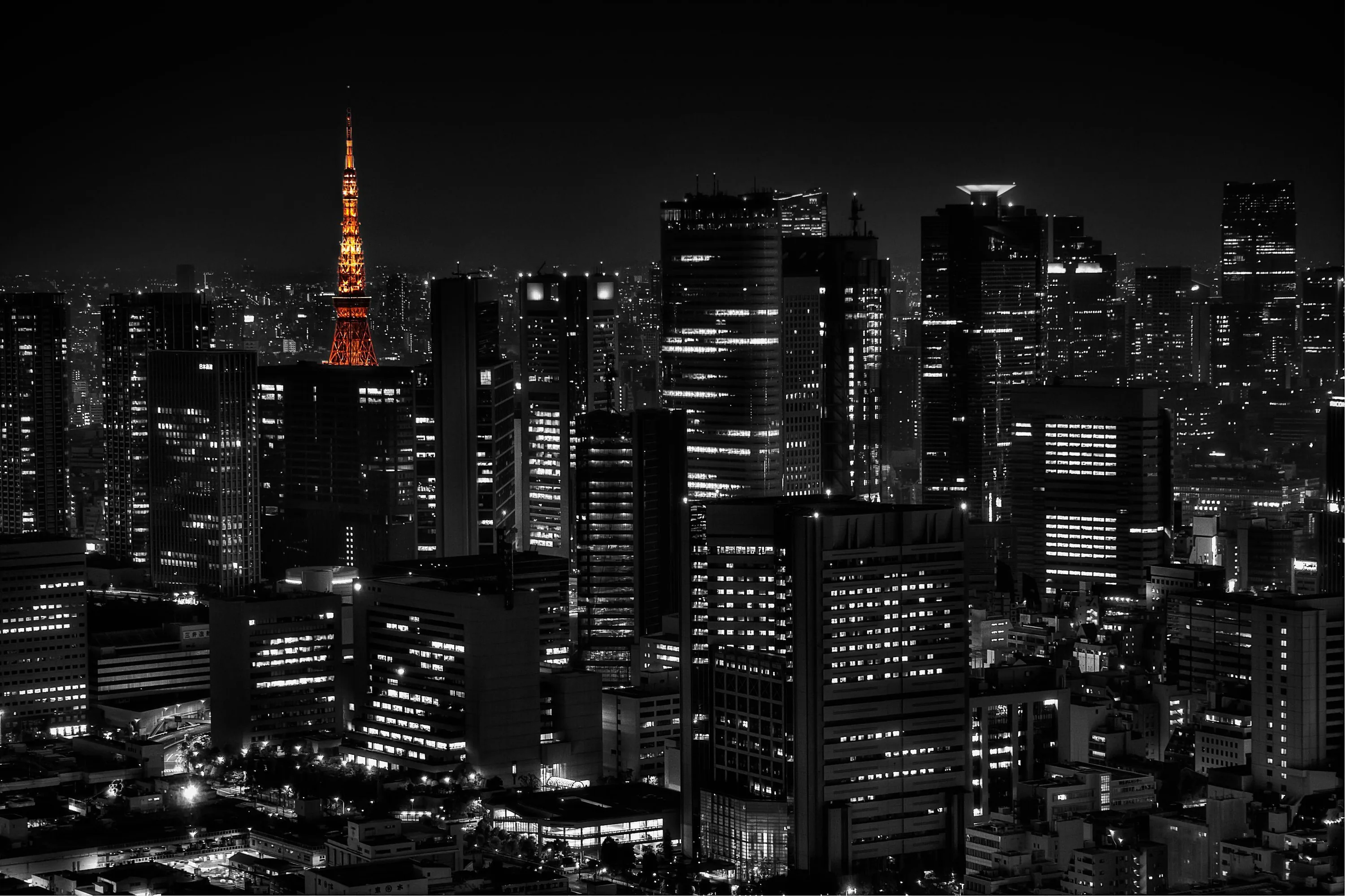 Tokyo Tower burns orange above an otherwise desaturated skyline at night, thousands of lit windows speckling the black towers around it.