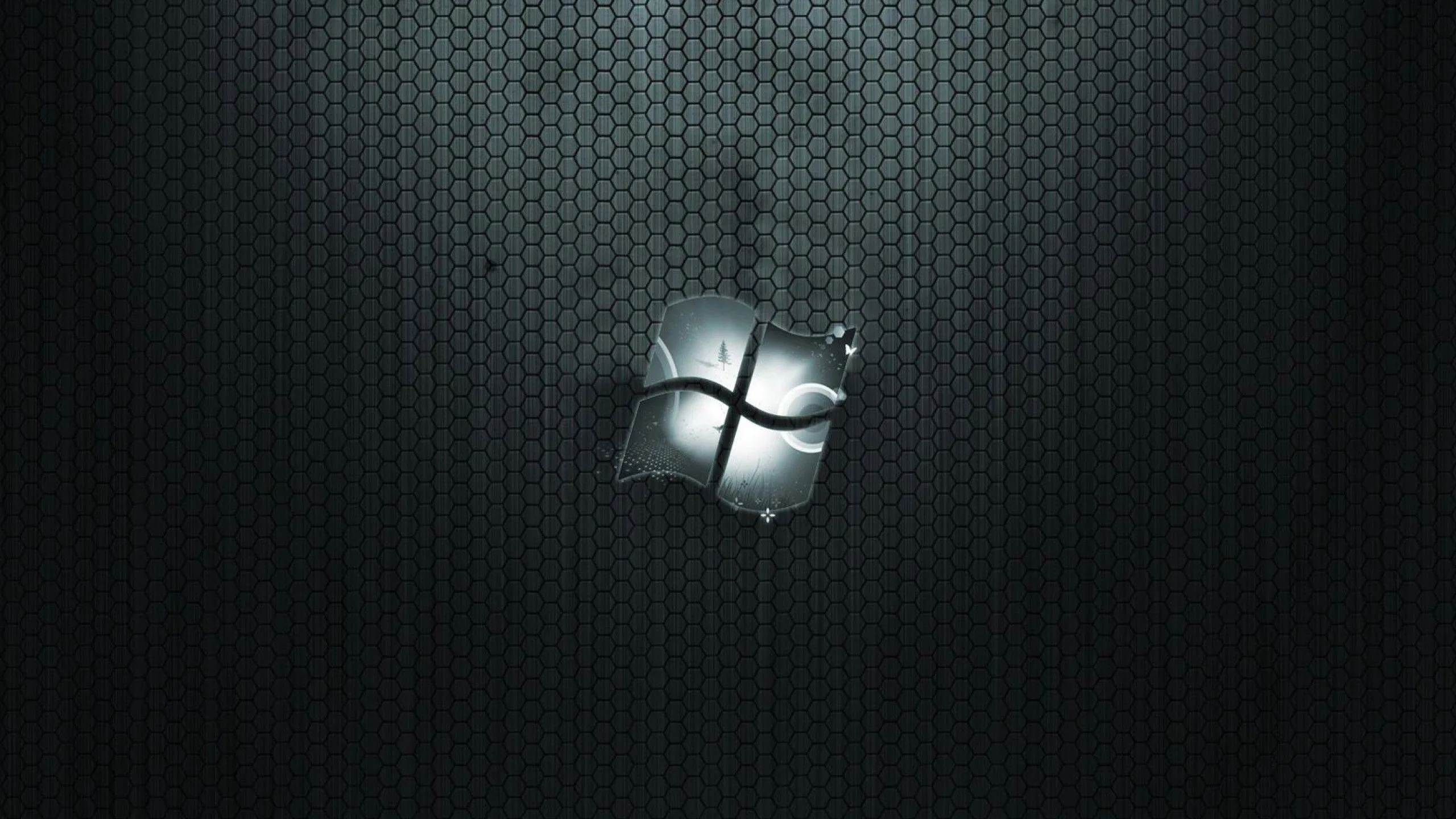 A brushed metal Windows emblem hangs at the centre of a dark honeycomb mesh panel, light falling off sharply toward the corners.