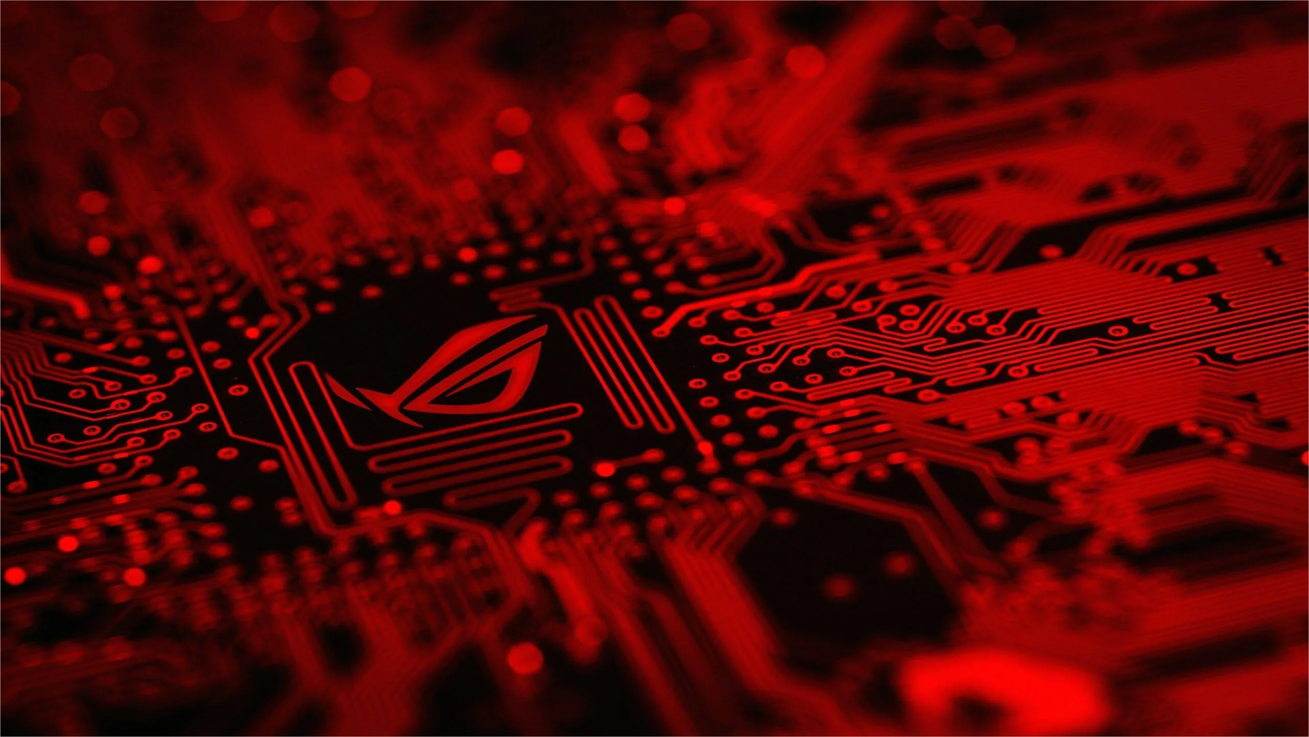 The ASUS Republic of Gamers eye glows above a motherboard packed with chips and traces, everything washed in hard red light.