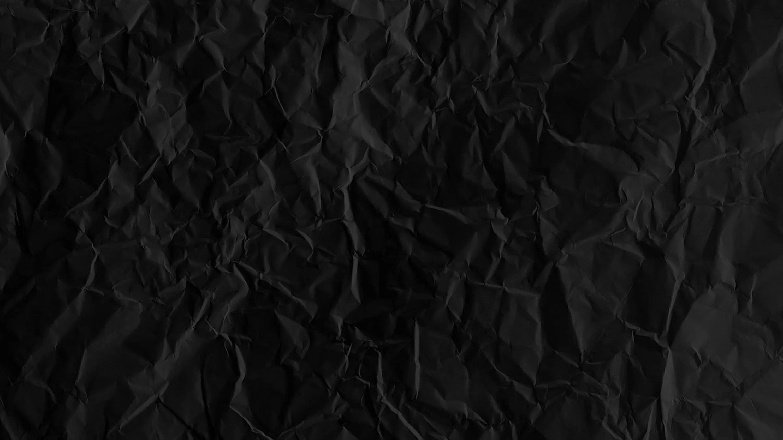 A sheet of black paper crumpled into shallow creases, every fold edge catching the same soft light so the surface stays even behind icons.